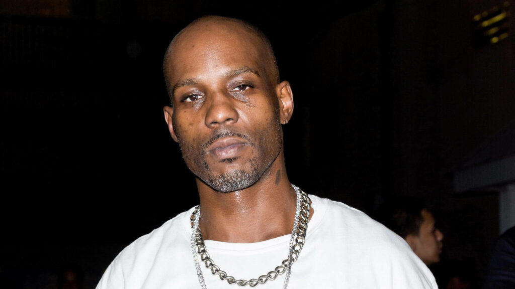 Close-up of DMX rapper with intense gaze bald head chain necklace urban dark background wallpaper