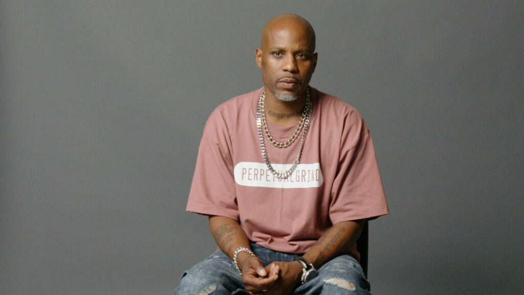 DMX rapper in pink shirt and chains sitting against gray background reflecting music legacy Wallpaper