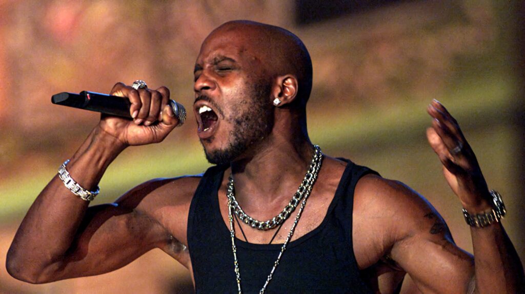 DMX performing passionately with microphone chains muscular physique warm dramatic lighting wallpaper