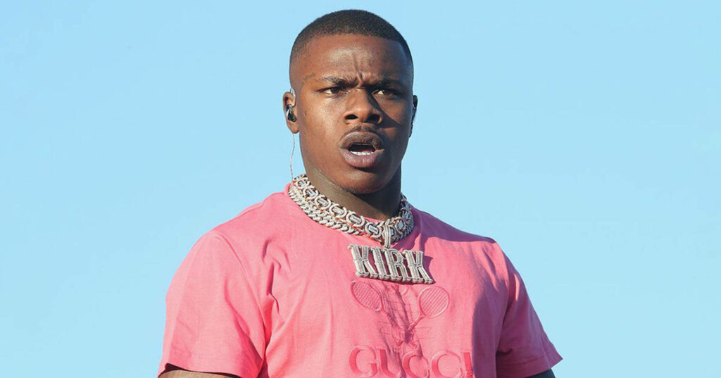 DaBaby on stage wearing vibrant pink shirt silver chains energetic performance blue sky wallpaper