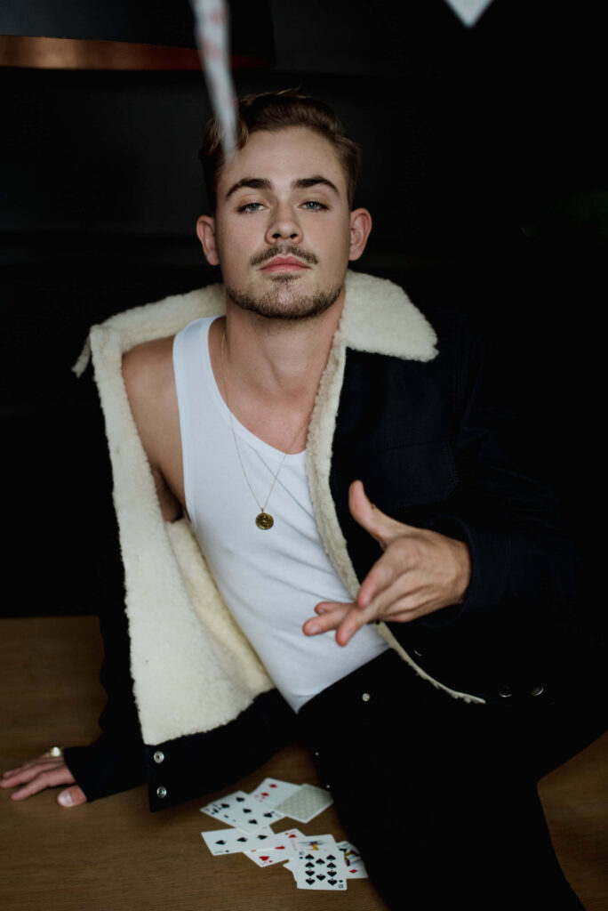 Dacre Montgomery moody portrait wearing shearling jacket and white tank top with playing cards Wallpaper