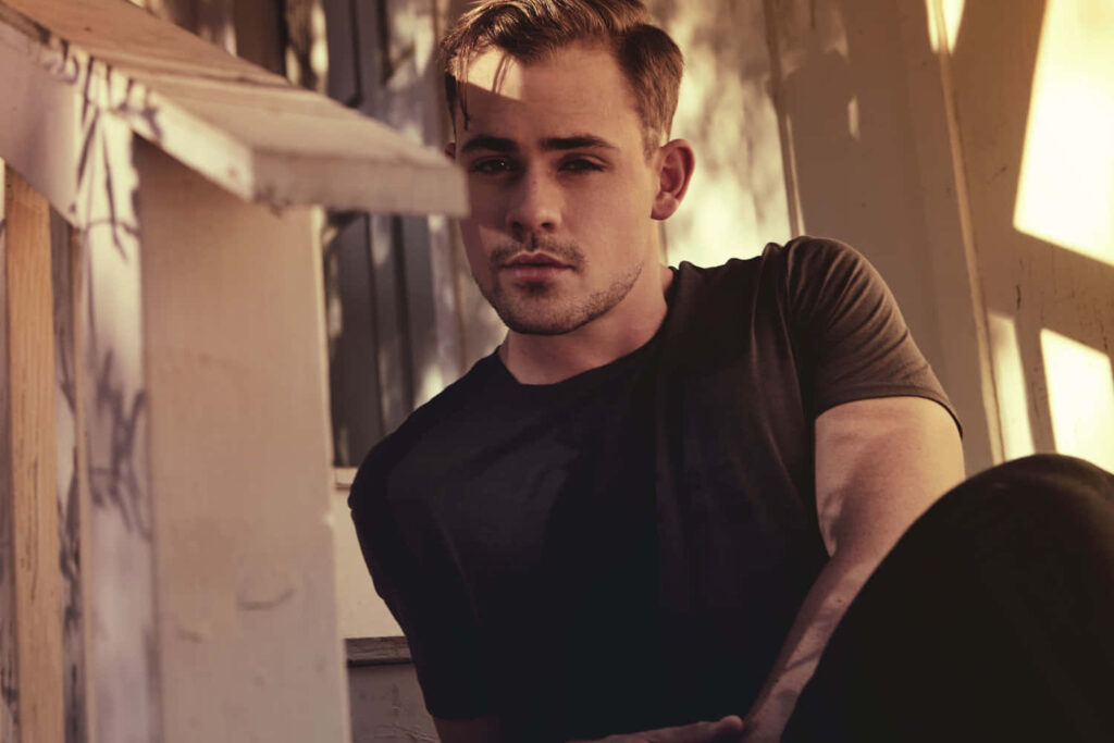 Dacre Montgomery in warm natural light wearing dark shirt relaxed pose sunlit earthy tones wallpaper