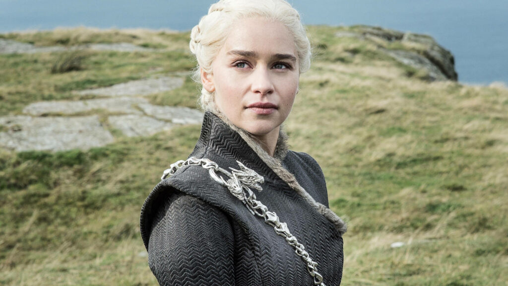 Emilia Clarke as Daenerys Targaryen stands on rugged landscape with platinum hair and dark attire Wallpaper
