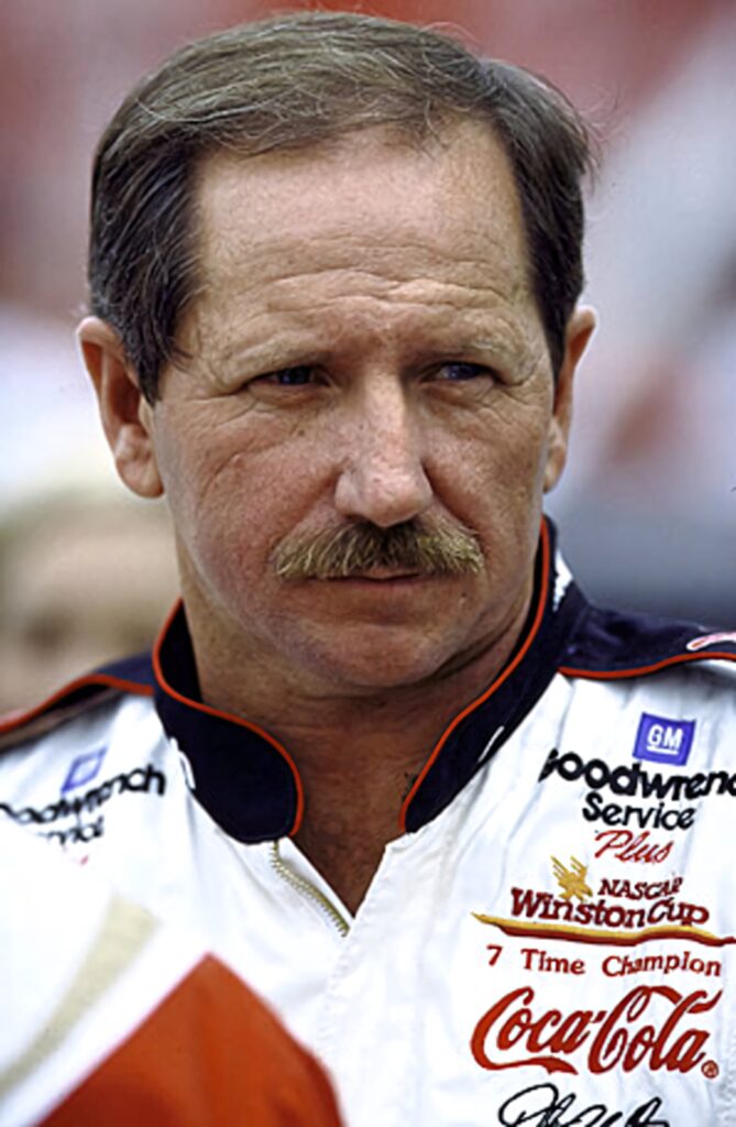 Dale Earnhardt in Coca-Cola racing suit focused at NASCAR track with vibrant motorsport colors Wallpaper