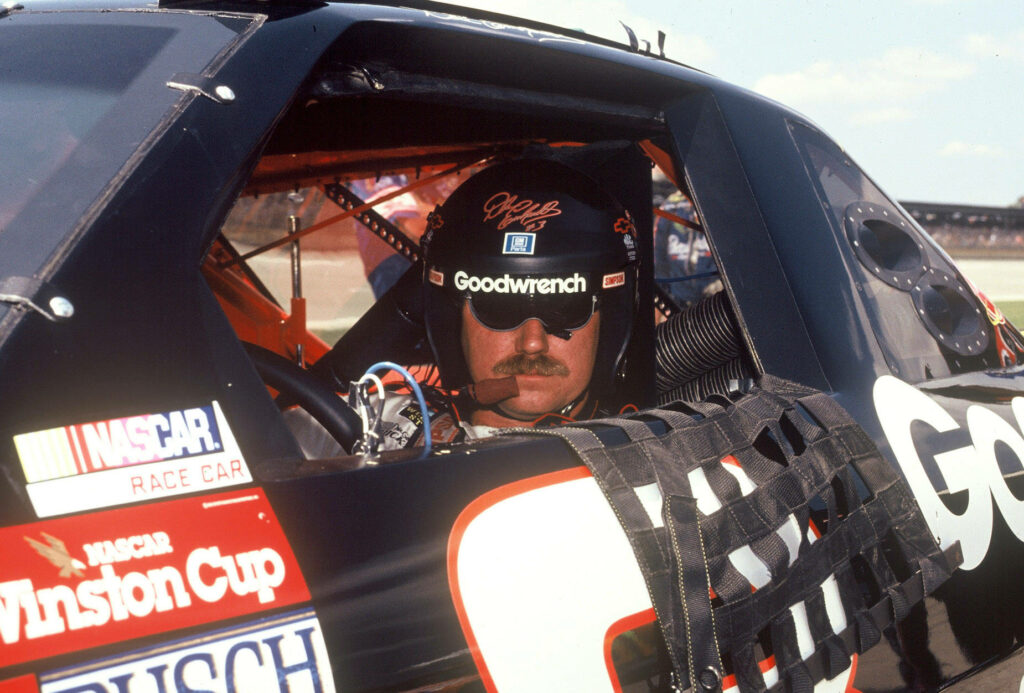 Dale Earnhardt focused in race car wearing helmet sunglasses surrounded by sponsor logos black red Wallpaper