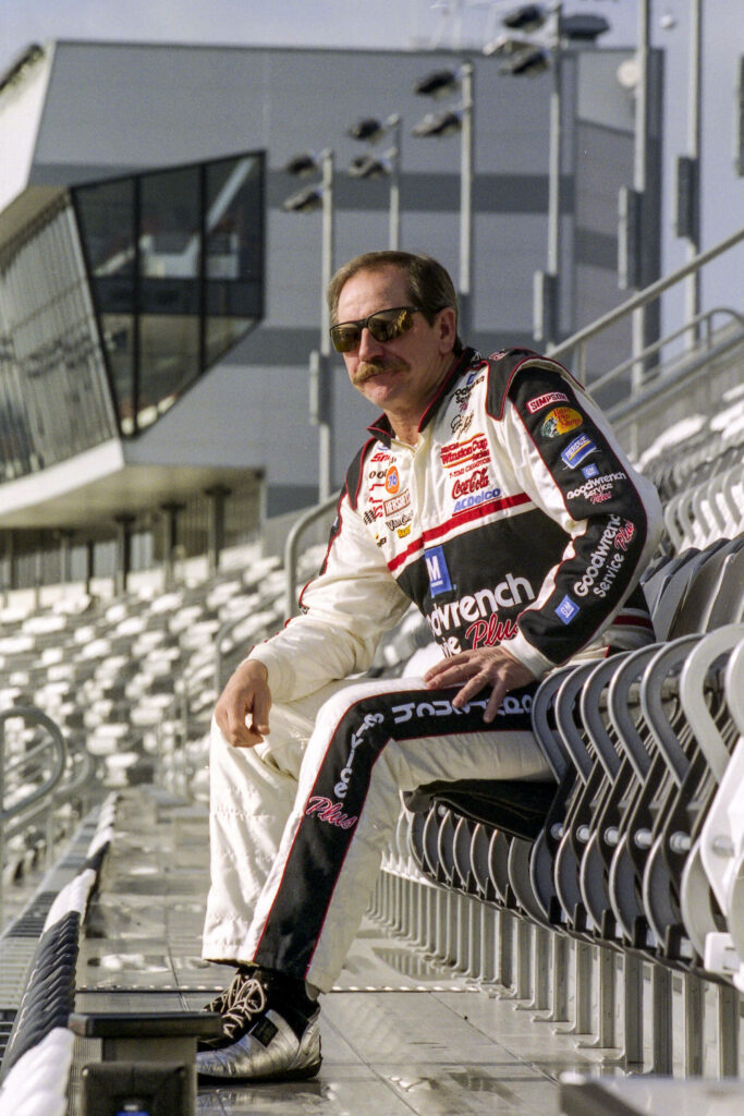 Dale Earnhardt in racing suit sitting on bench in empty stadium reflecting calm mood and focus Wallpaper