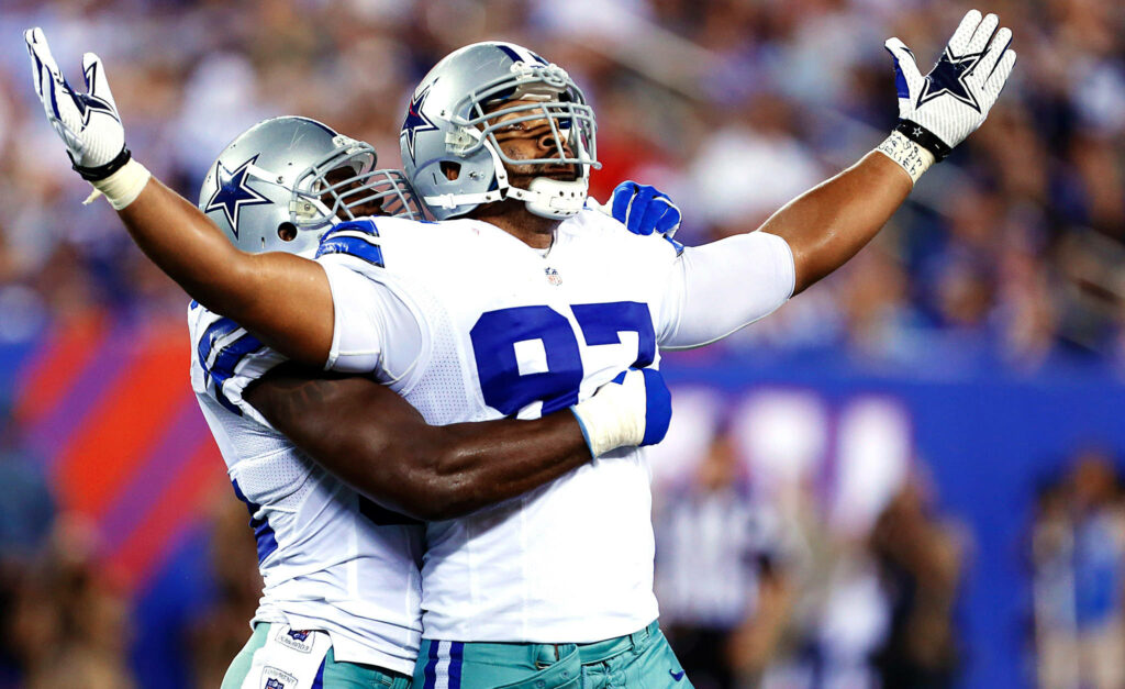 Dallas Cowboys player in silver blue uniform celebrates on field with teammate vibrant football game Wallpaper