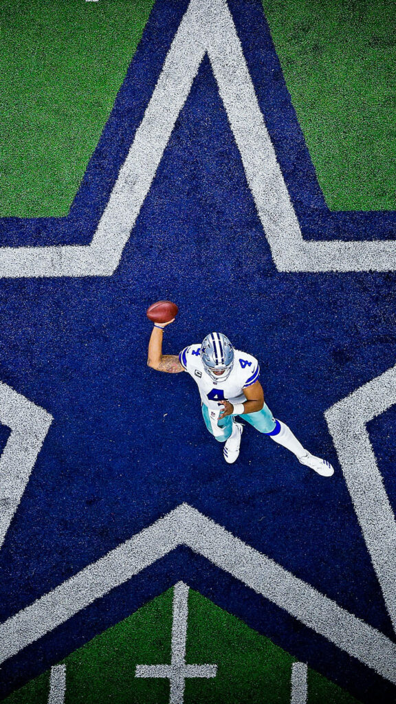 Dallas Cowboys player throwing football on star at midfield with bright green turf background Wallpaper