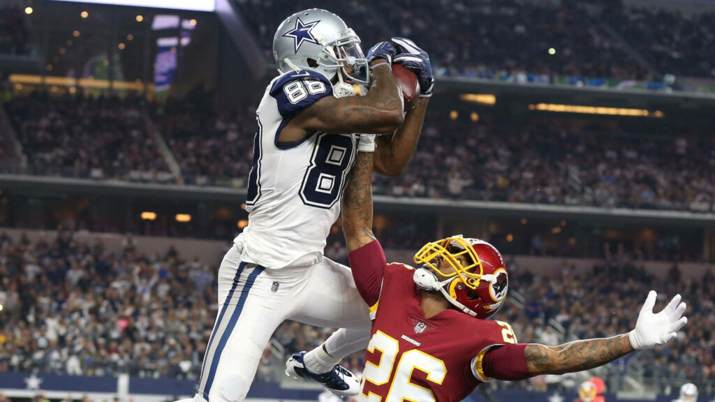 Dallas Cowboys player mid-air catching football over Washington defender in packed stadium action Wallpaper