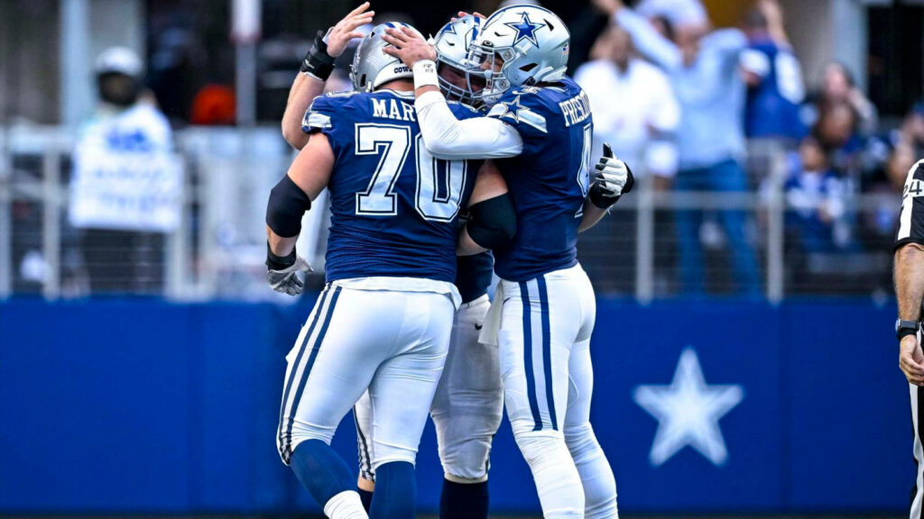 Dallas Cowboys players in navy and silver uniforms share team hug on field showing unity and teamwork Wallpaper