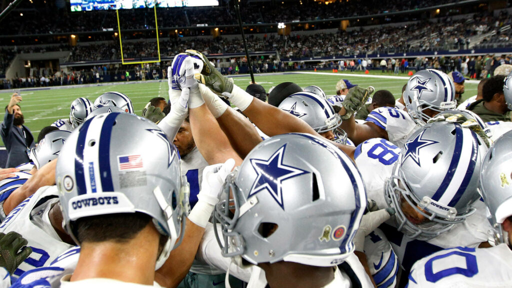 Dallas Cowboys team huddled in silver blue helmets under stadium lights showing unity and strength Wallpaper