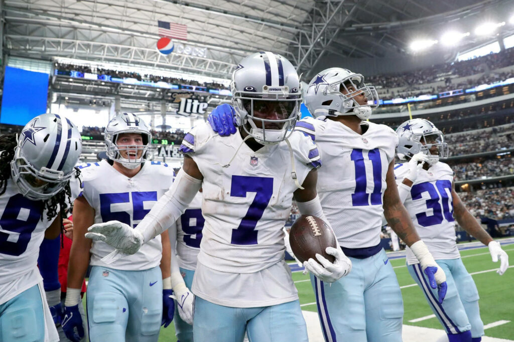 Dallas Cowboys players in silver and blue uniforms walk united on field with bright stadium crowd Wallpaper