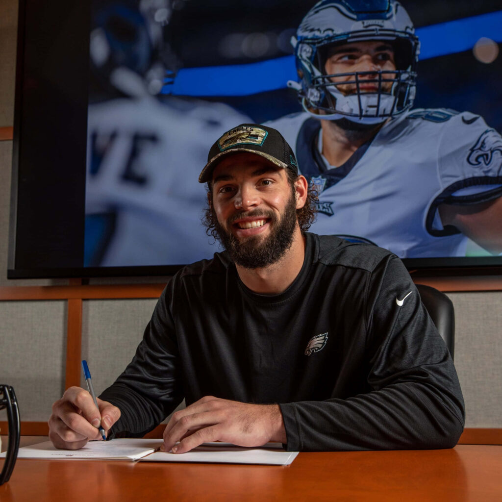 Dallas Goedert smiling signing Philadelphia Eagles contract with vibrant action wallpaper background
