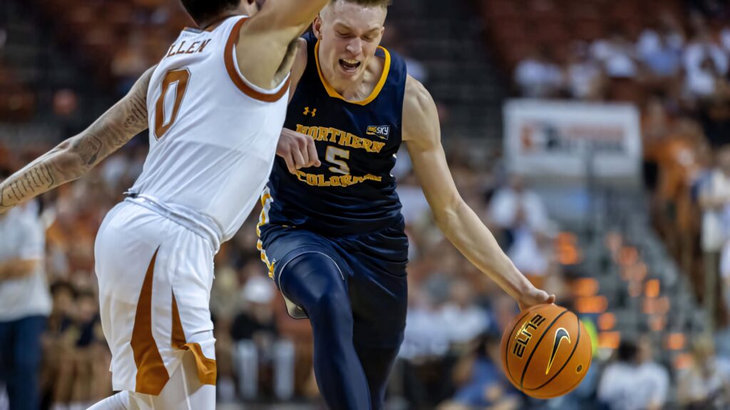 Dalton Knecht dribbling past defender in intense basketball game with vibrant team colors Wallpaper