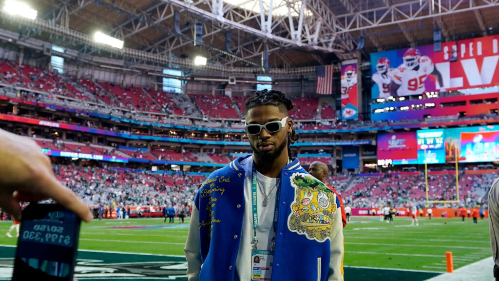 Damar Hamlin in blue jacket and white sunglasses on vibrant football field with crowded red stadium seats Wallpaper