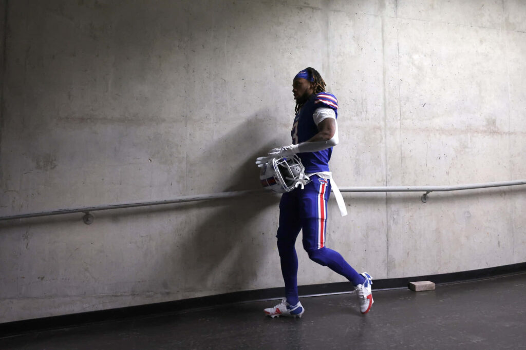 Damar Hamlin in blue football uniform walking alone through concrete tunnel holding helmet Wallpaper