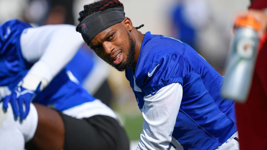 Damar Hamlin in blue jersey stretching during daylight football training with teammates outdoors Wallpaper