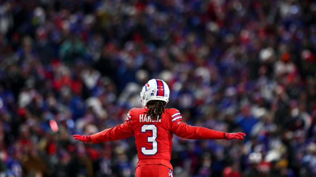 Damar Hamlin in red football uniform celebrates on field with vibrant stadium crowd background Wallpaper