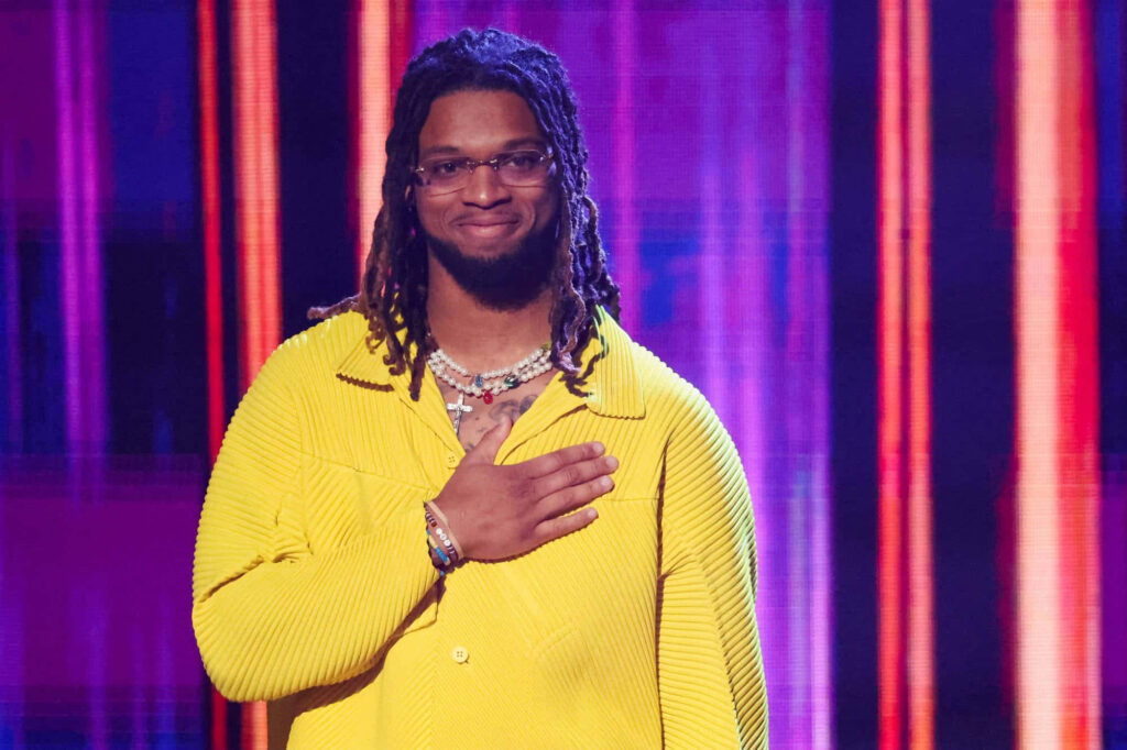 Damar Hamlin in bright yellow jacket with hand over heart against vibrant colorful backdrop Wallpaper