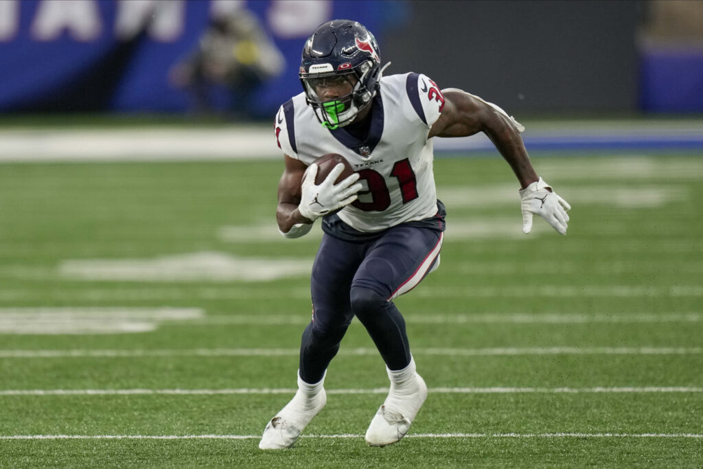 Dameon Pierce NFL running back in Houston Texans uniform carrying football on vibrant green field Wallpaper