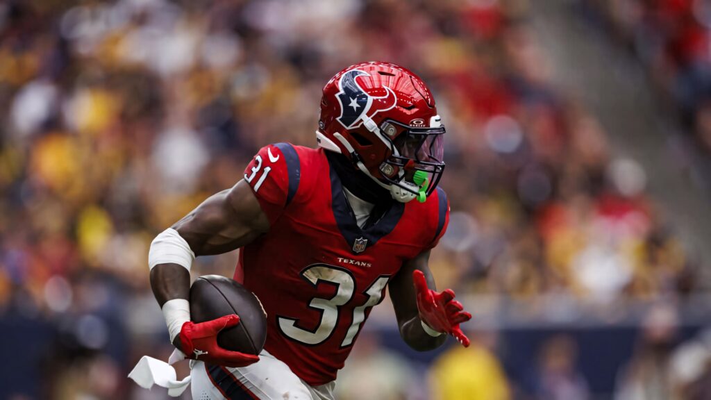 Dameon Pierce Houston Texans running back sprinting in red blue uniform with blurred stadium background Wallpaper