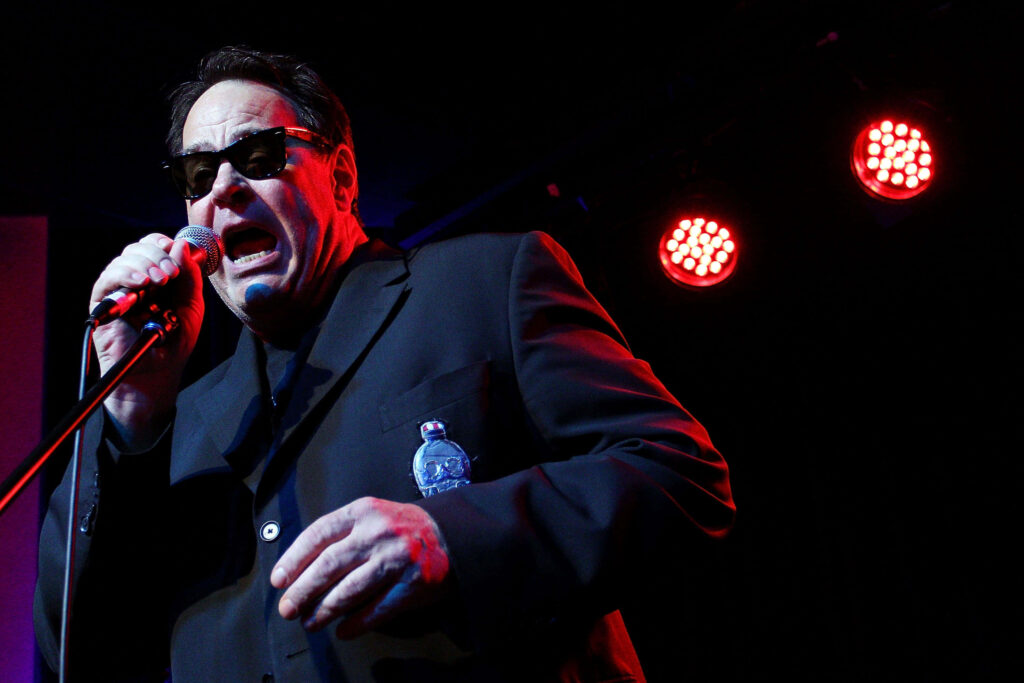 Dan Aykroyd performing on stage in black suit and sunglasses with red dramatic lighting wallpaper