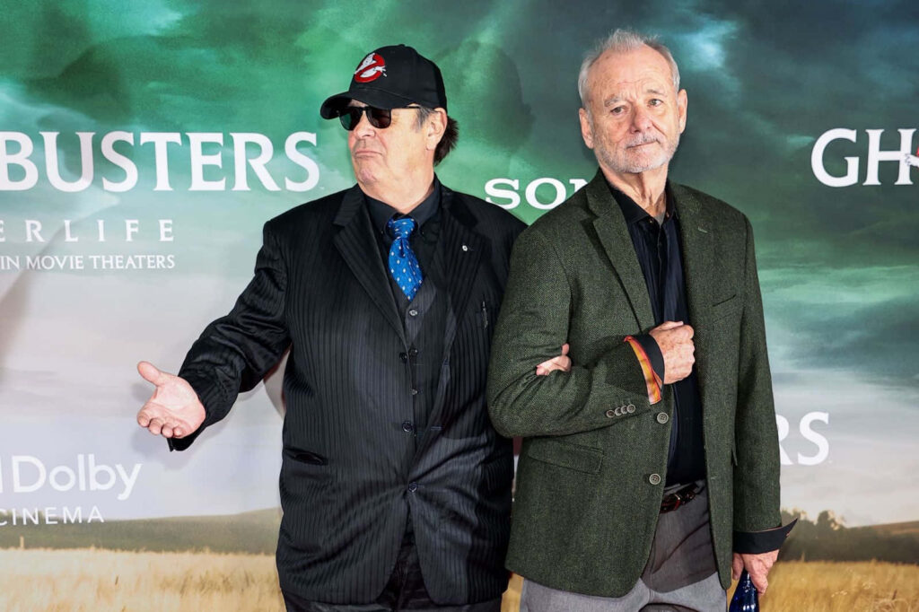 Dan Aykroyd and Bill Murray at Ghostbusters event dressed formally with themed backdrop wallpaper
