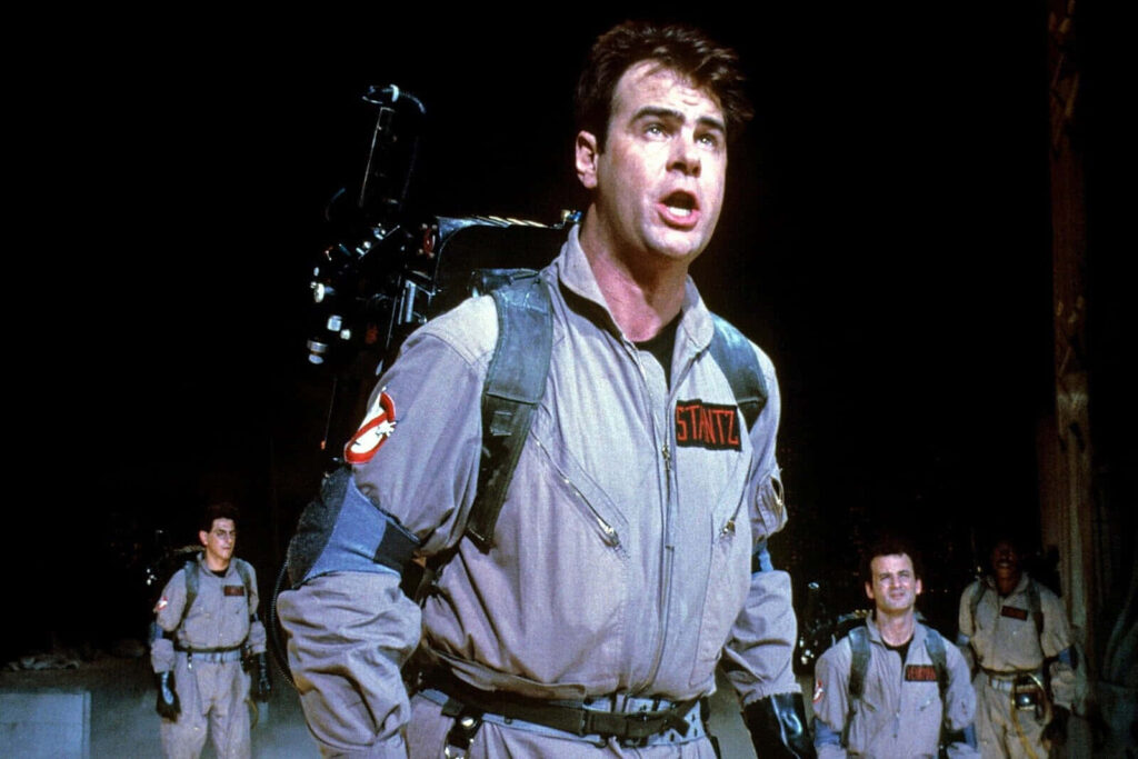 Dan Aykroyd as Ray Stantz in Ghostbusters uniform with proton pack against city backdrop wallpaper