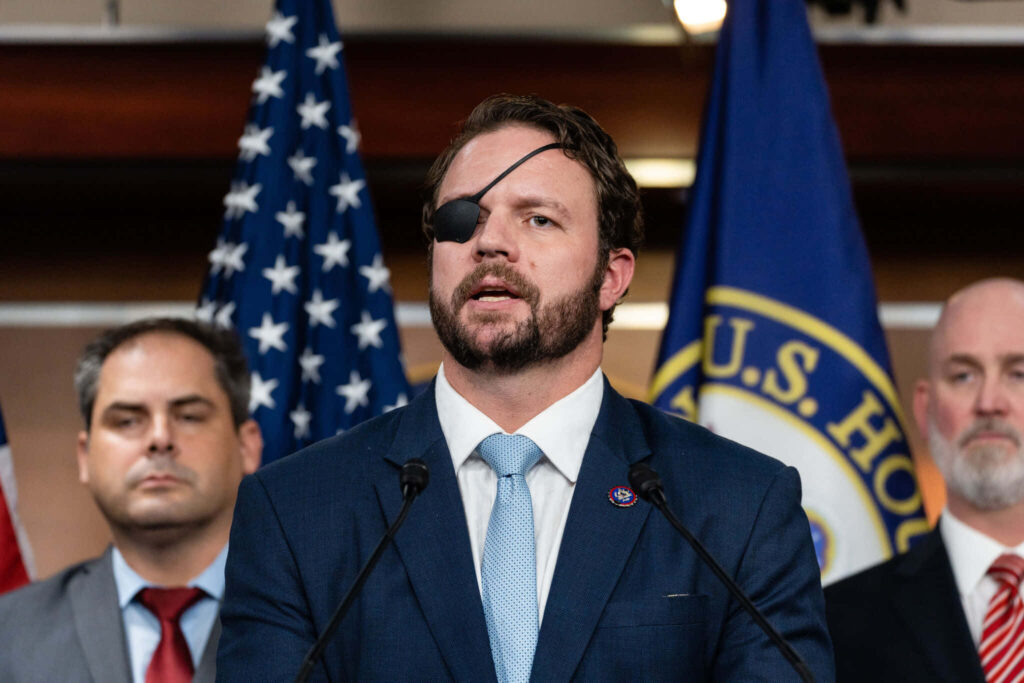 Dan Crenshaw confident at podium wearing eyepatch dark suit with American flags political setting Wallpaper