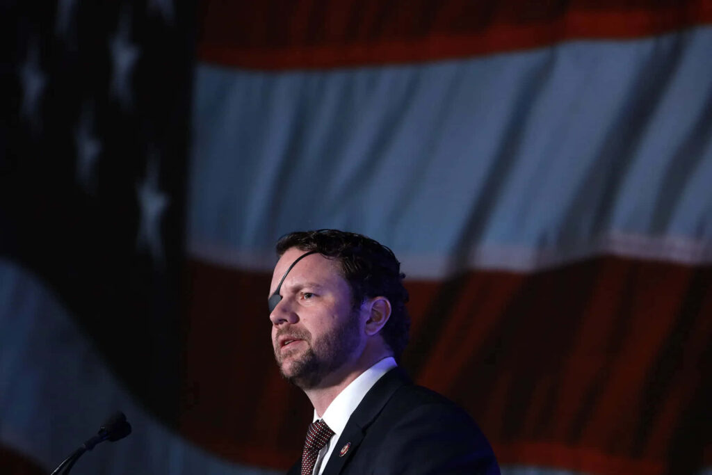 Dan Crenshaw in suit with eye patch standing against dramatic American flag patriotic background Wallpaper