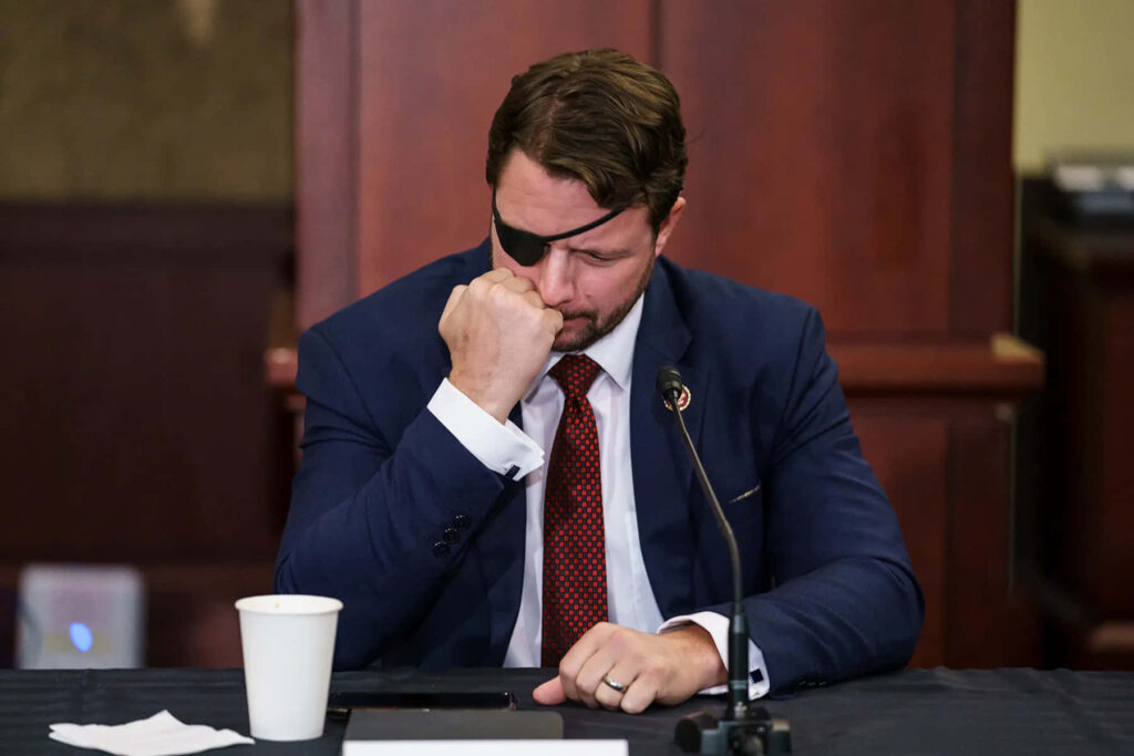 Dan Crenshaw in navy suit with eyepatch seated at table with coffee and documents serious tone Wallpaper