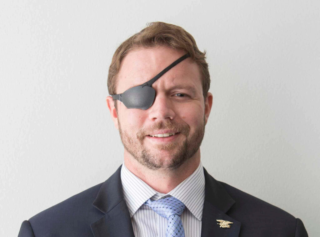 Portrait of Dan Crenshaw in dark suit and blue tie with black eye patch and confident smile Wallpaper