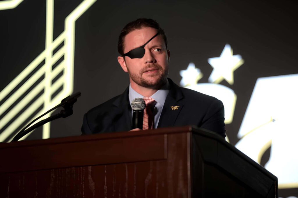 Dan Crenshaw at podium wearing suit and eyepatch with bold geometric background wallpaper