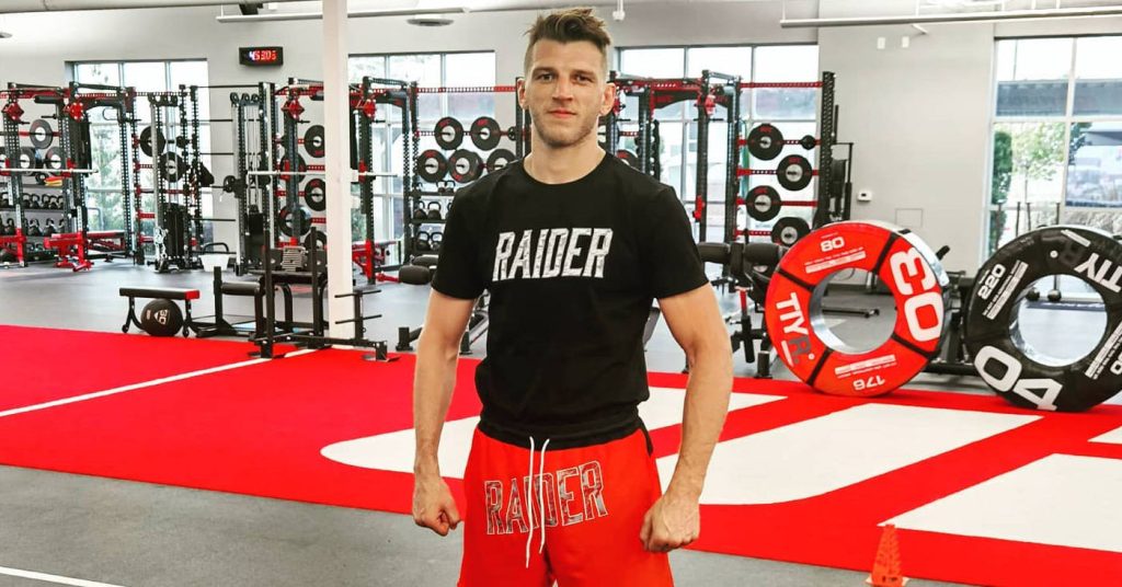 UFC fighter Dan Hooker in black Raider shirt and red shorts posing in bright gym background Wallpaper