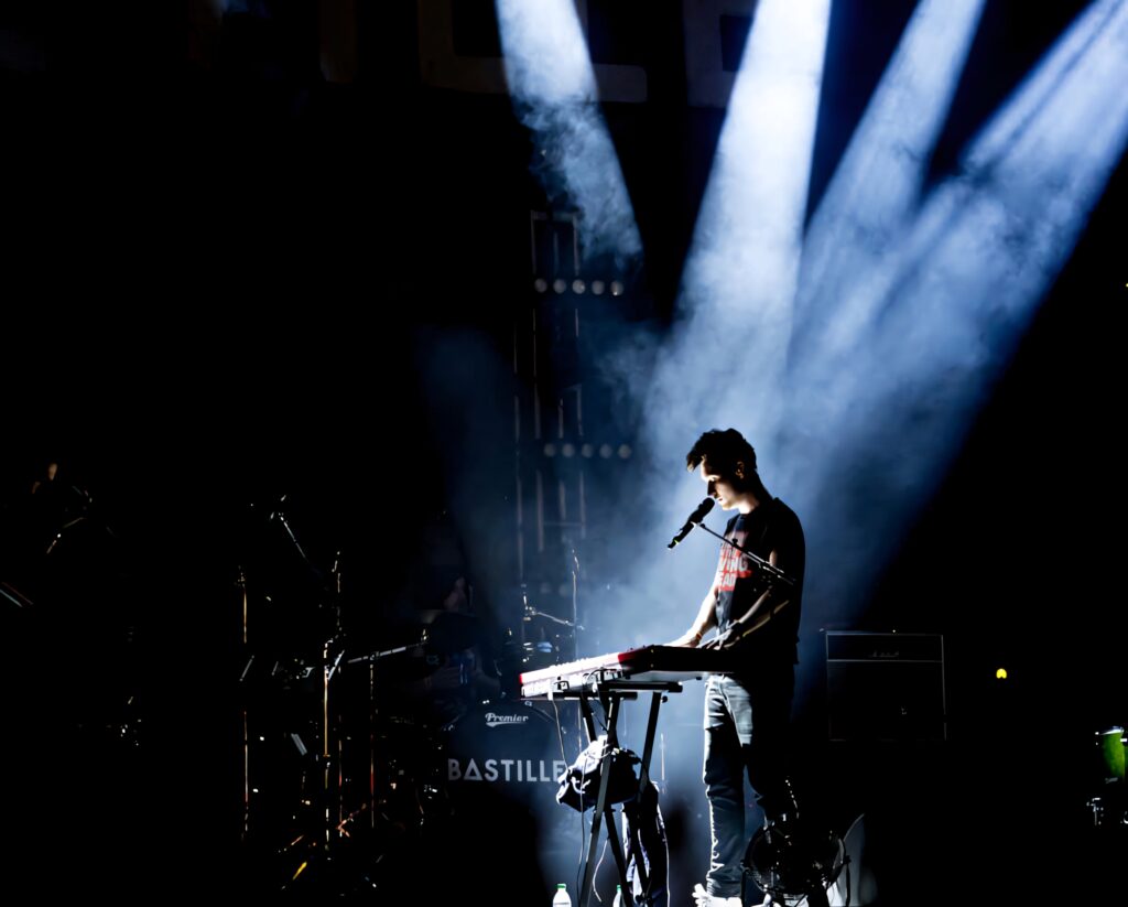 Dan Smith of Bastille singing live on stage with dramatic spotlights capturing energy and emotion Wallpaper