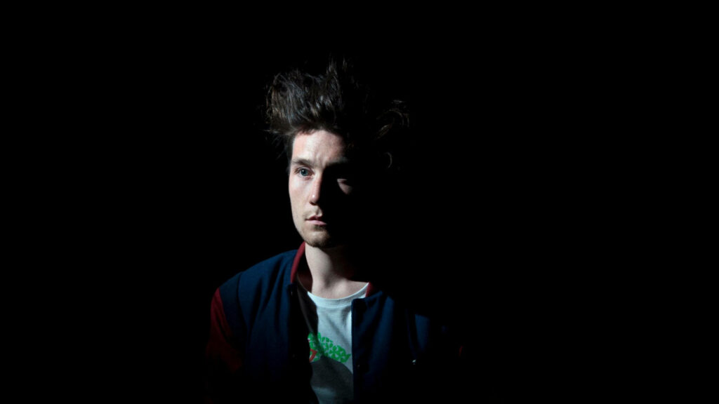 Dan Smith of Bastille in moody dramatic lighting against dark background intense wallpaper background