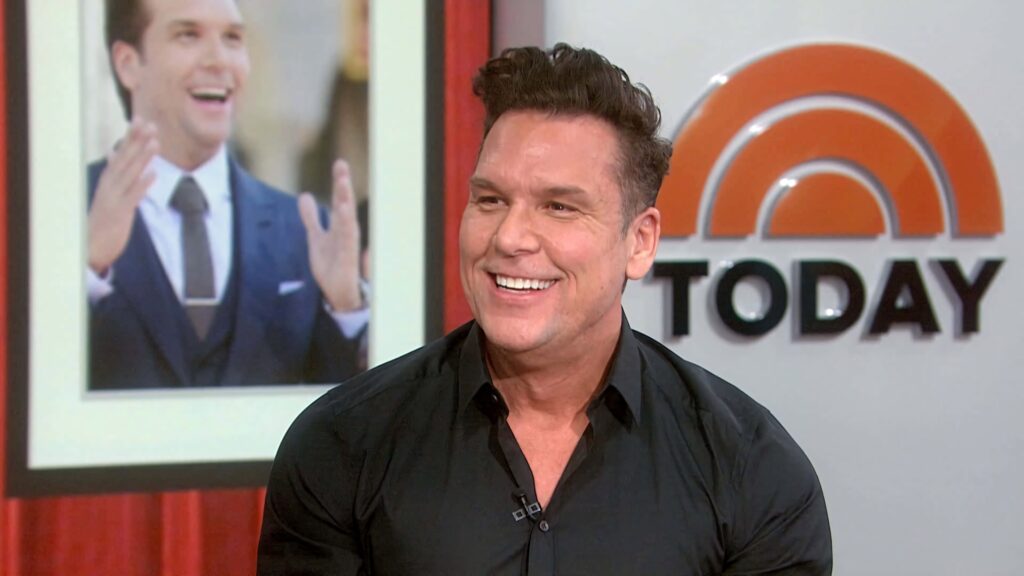 Dane Cook smiling confidently during vibrant TODAY show interview in warm orange studio background Wallpaper