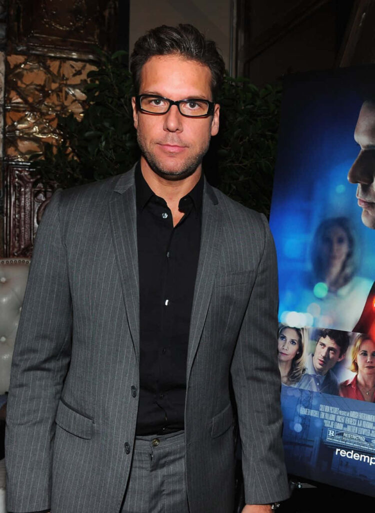 Dane Cook in gray pinstripe suit with black shirt at event with vibrant blue red movie poster background Wallpaper
