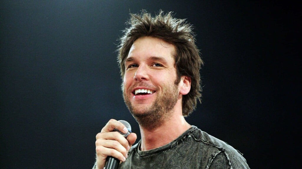 Dane Cook smiling confidently holding microphone vibrant live performance wallpaper background