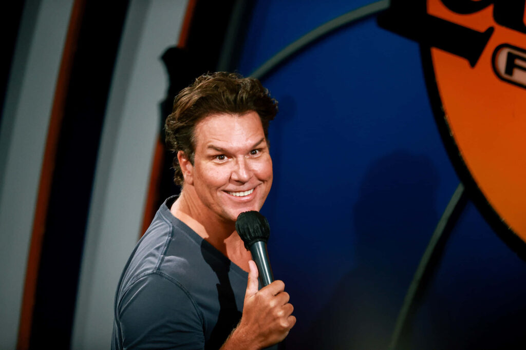Dane Cook performing energetic stand-up comedy with vibrant blue orange stage background wallpaper