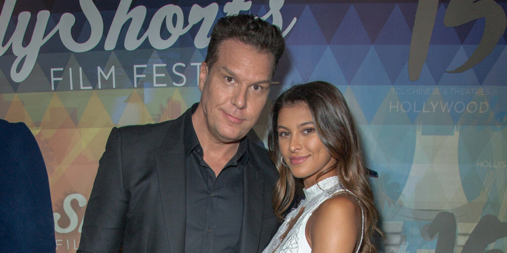 Dane Cook and wife Kelsi Taylor in stylish formal attire at film festival with colorful geometric background Wallpaper