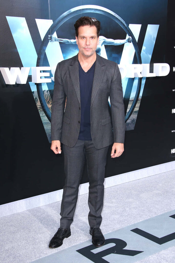 Dane Cook in dark tailored suit with sleek Westworld backdrop high contrast modern design wallpaper