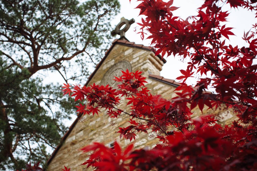 Danforth Chapel stone architecture framed by red maple leaves in autumn under cloudy sky Wallpaper