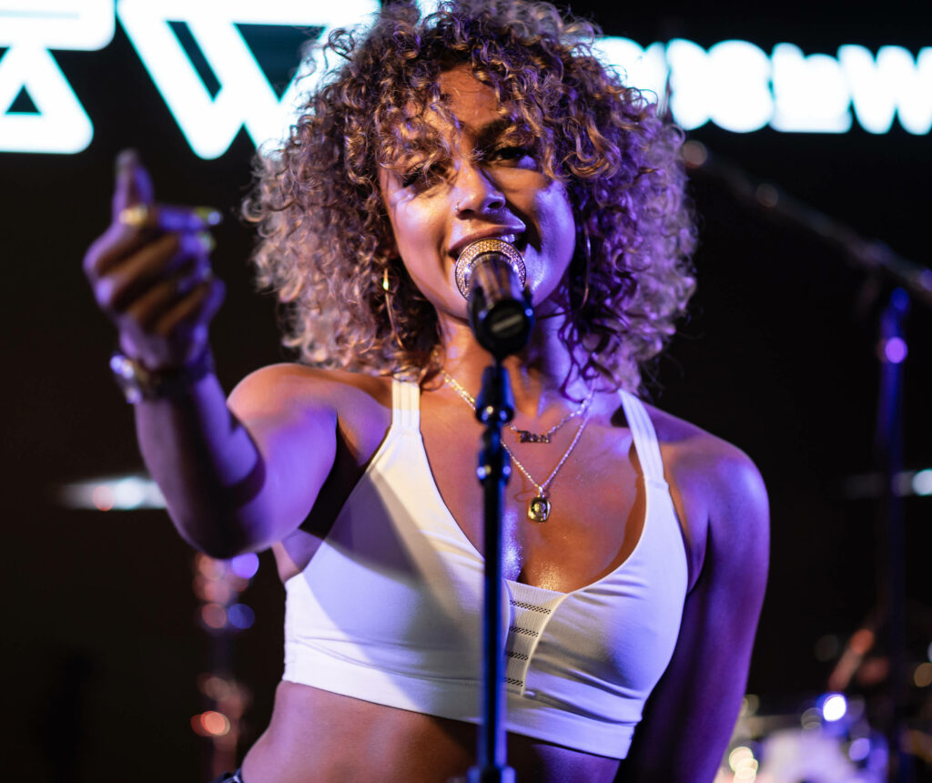 DaniLeigh performing on stage with vibrant purple gold lighting wearing white crop top and jewelry Wallpaper