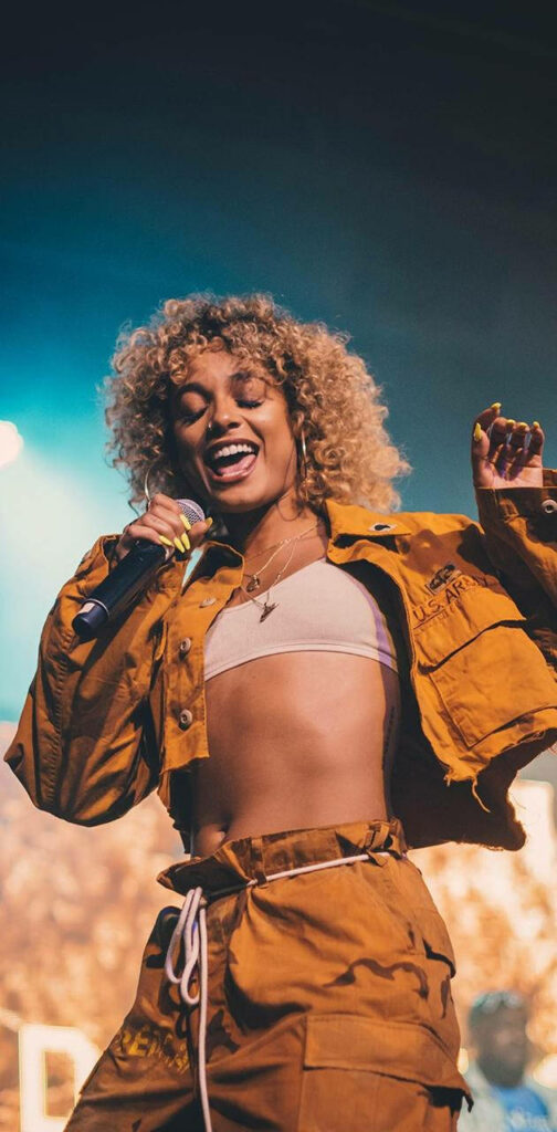 DaniLeigh vibrant stage performance in yellow outfit with natural curls on concert wallpaper
