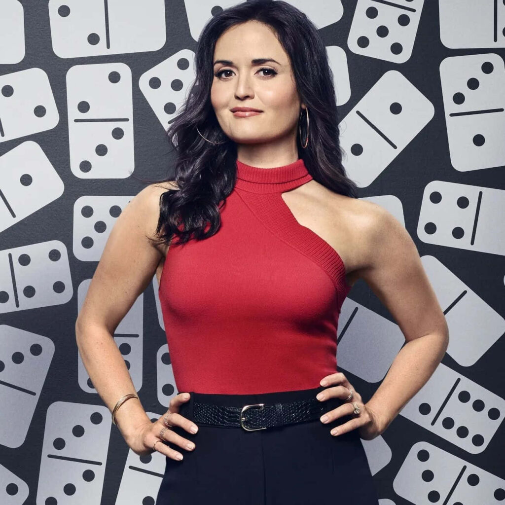 Danica McKellar confident pose red asymmetrical top black pants bold domino pattern background Wallpaper