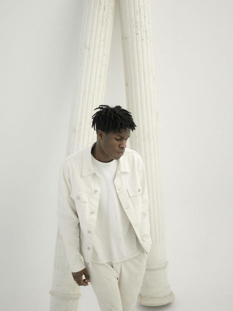 Daniel Caesar in all white outfit by tall white pillars calm minimalist modern wallpaper background