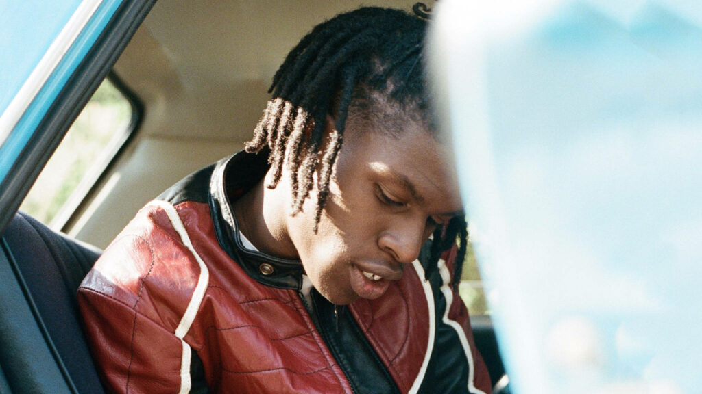 Daniel Caesar candid in car with braided hair red black leather jacket retro style wallpaper background