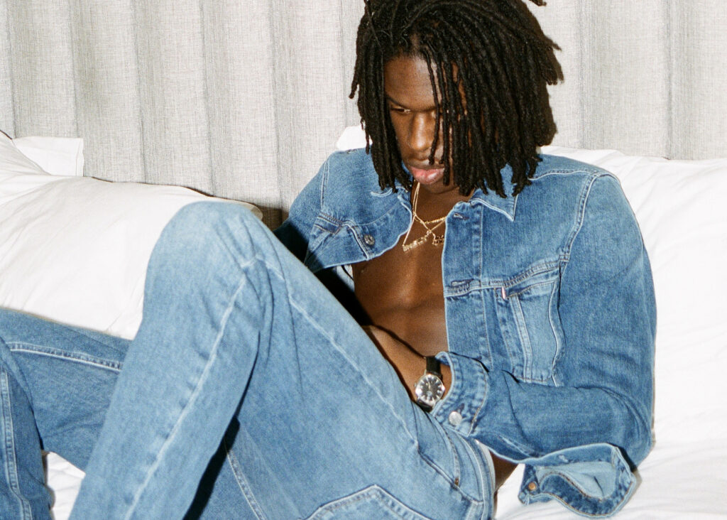 Daniel Caesar relaxed in denim jacket and jeans with soft natural light modern wallpaper background