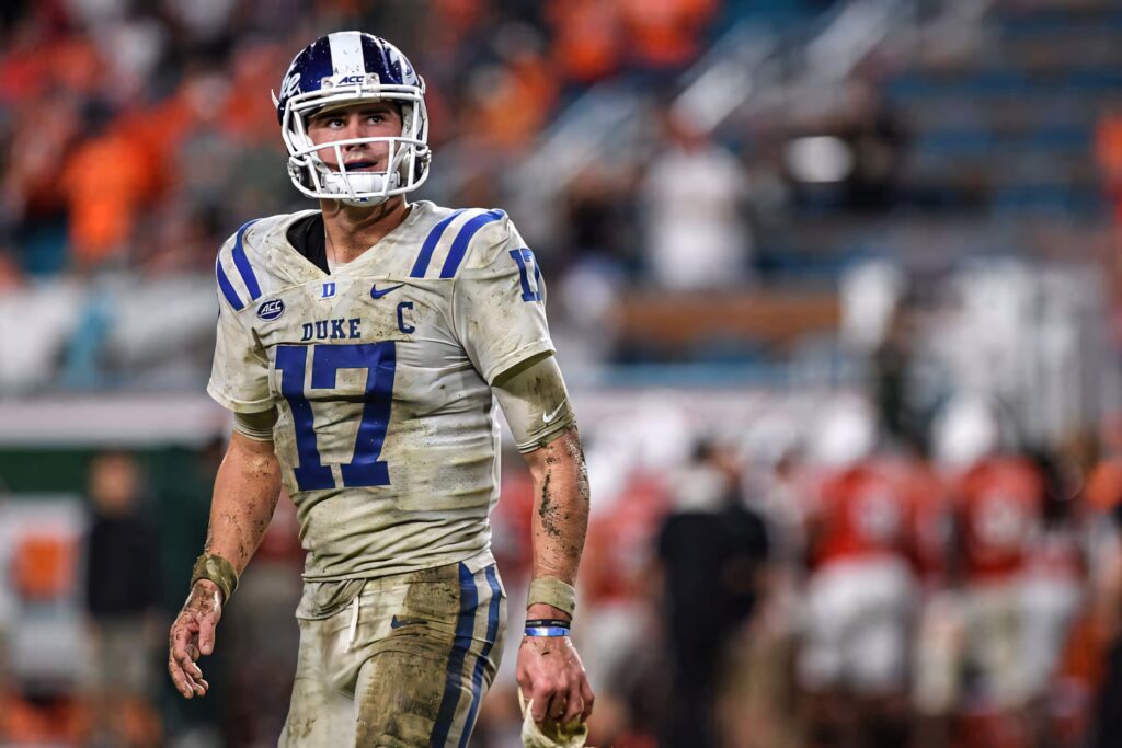 Daniel Jones Duke quarterback focused on field dirt marked jersey vibrant stadium lights crowd blur Wallpaper